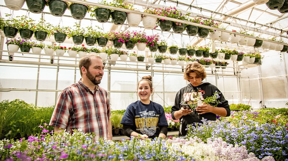 Teacher and two high school students working in a greenhouse with flowers